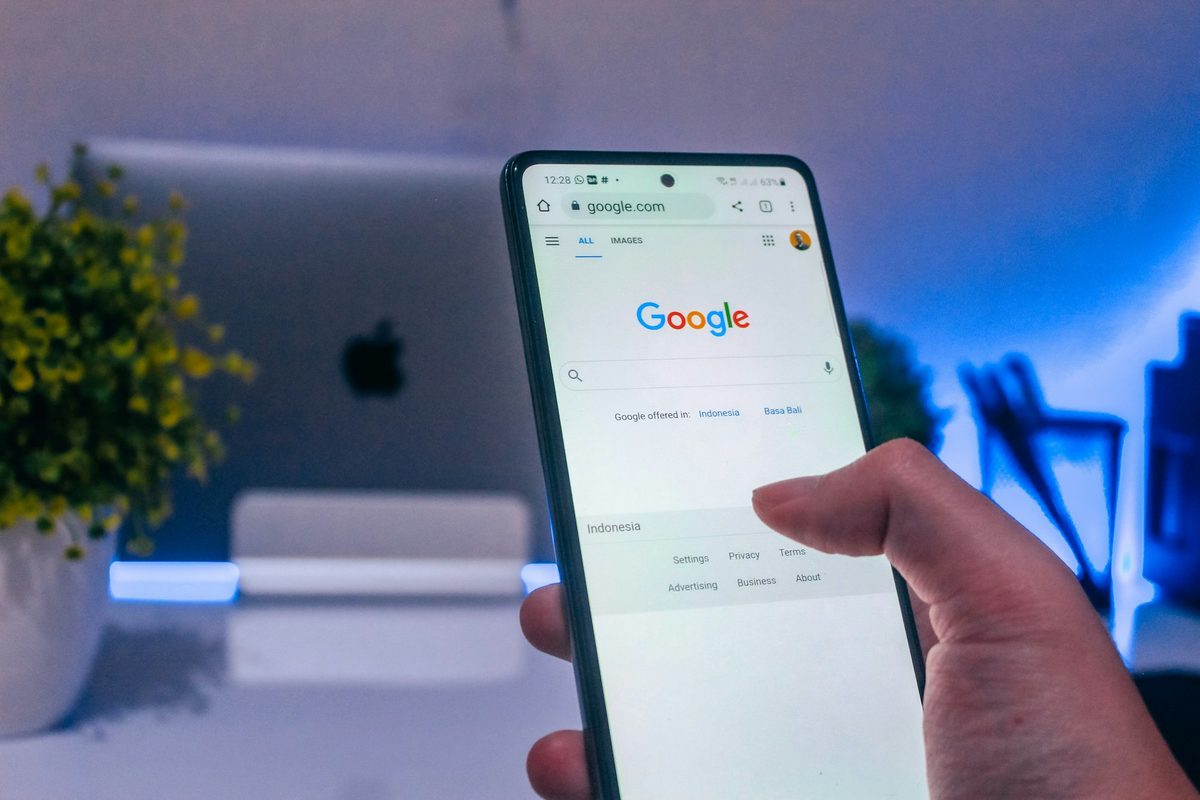 A hand holding a phone open on Google search, in front of a desk