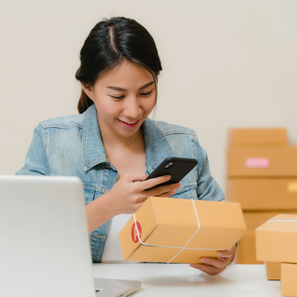 A shop owner checking an order on her phone beside a stack of parcels