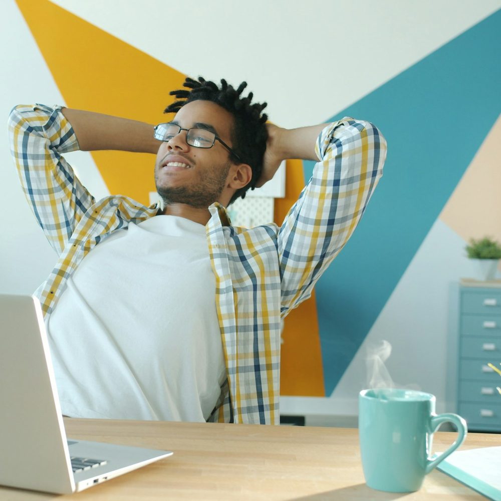 A man leaning back from his laptop with his hands behind his head